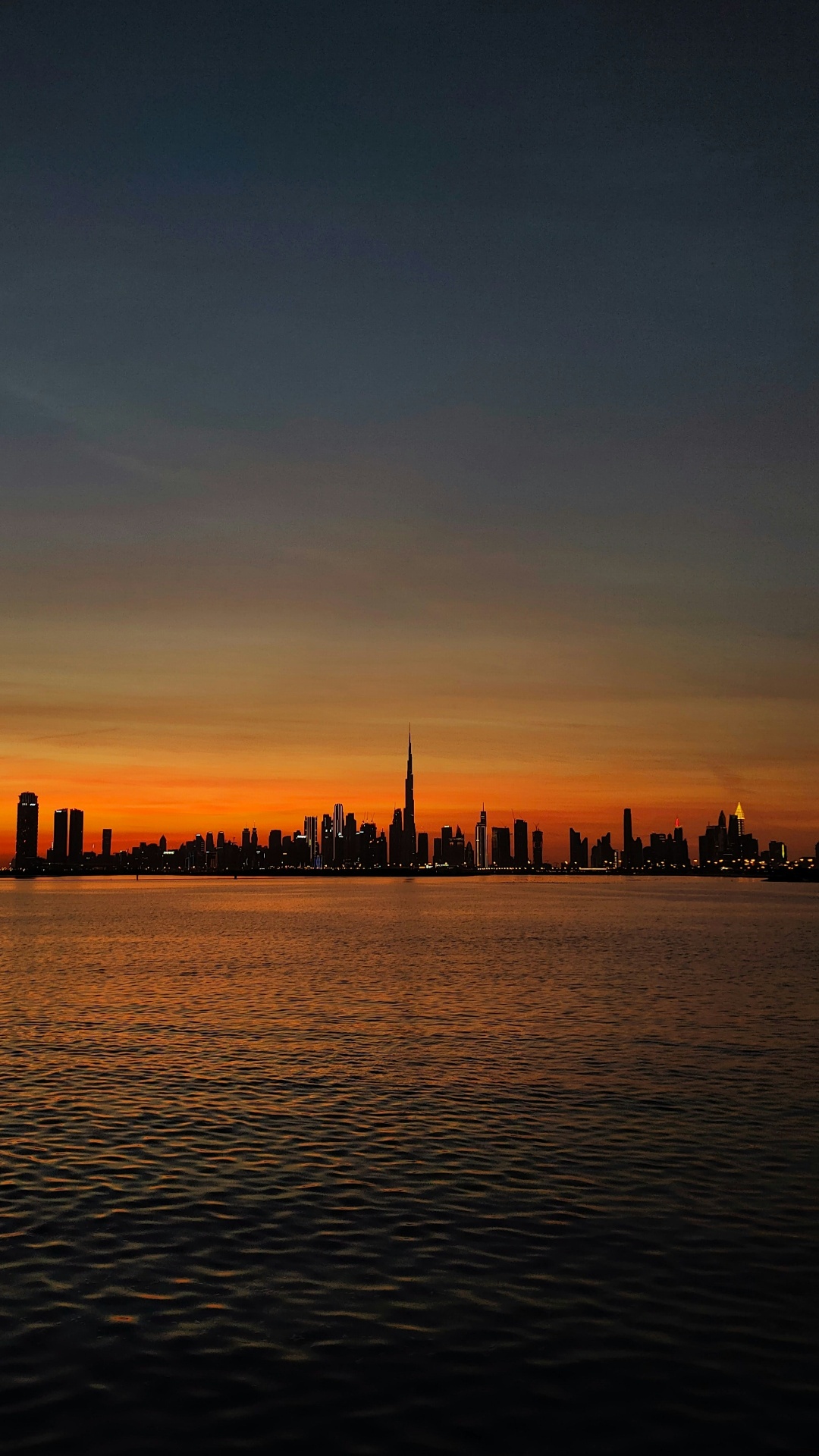 Dubai skyline silhouette at sunset across the water with Burj Khalifa